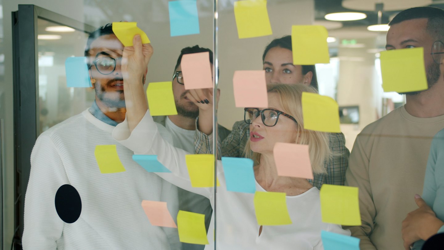 Zakelijk team brainstormt met post-its op glazen wand.