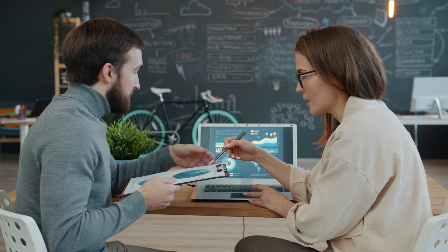 Twee zakelijke mensen bespreken gegevens op een laptop en een document.